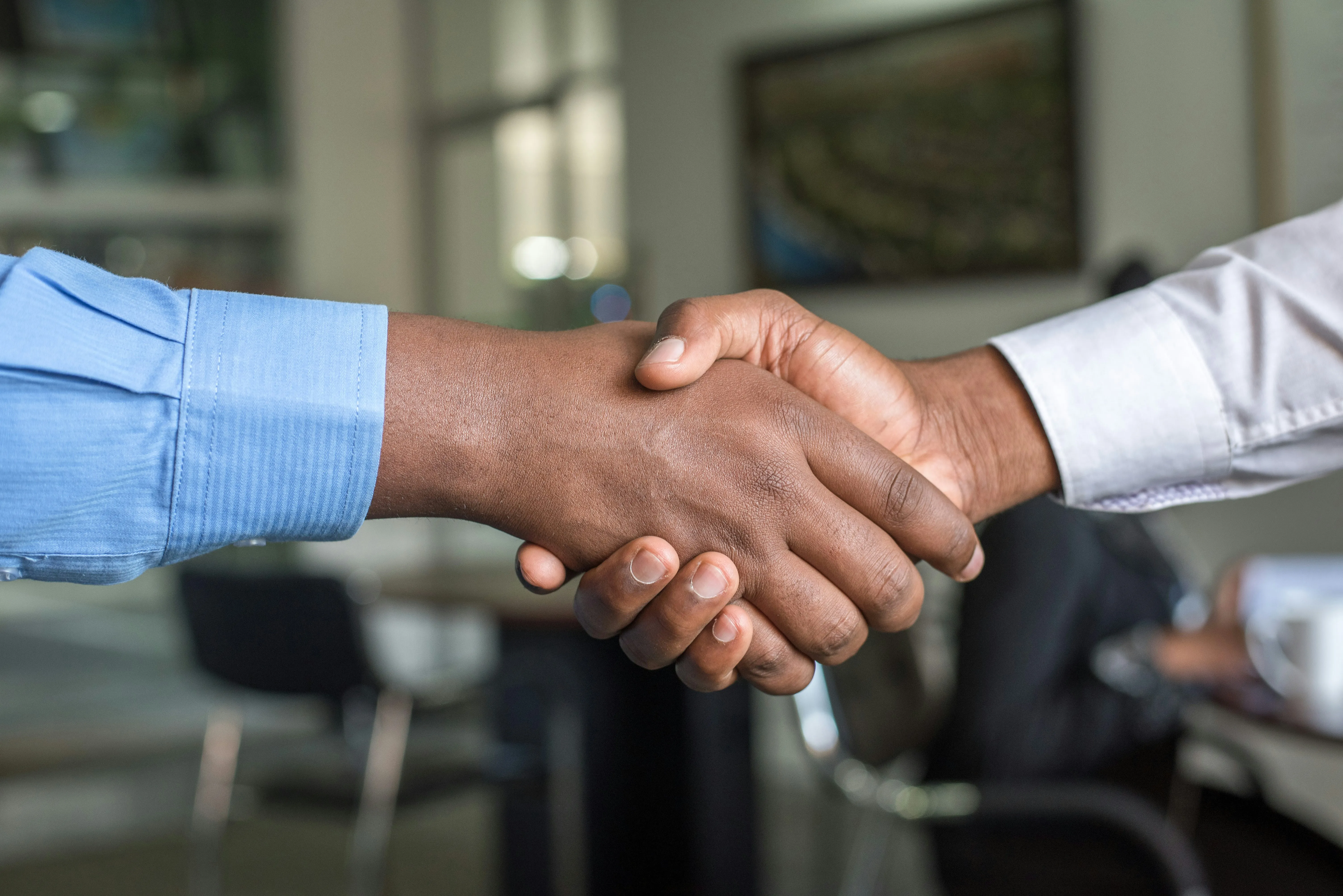Two people shaking hands across a meeting room table.