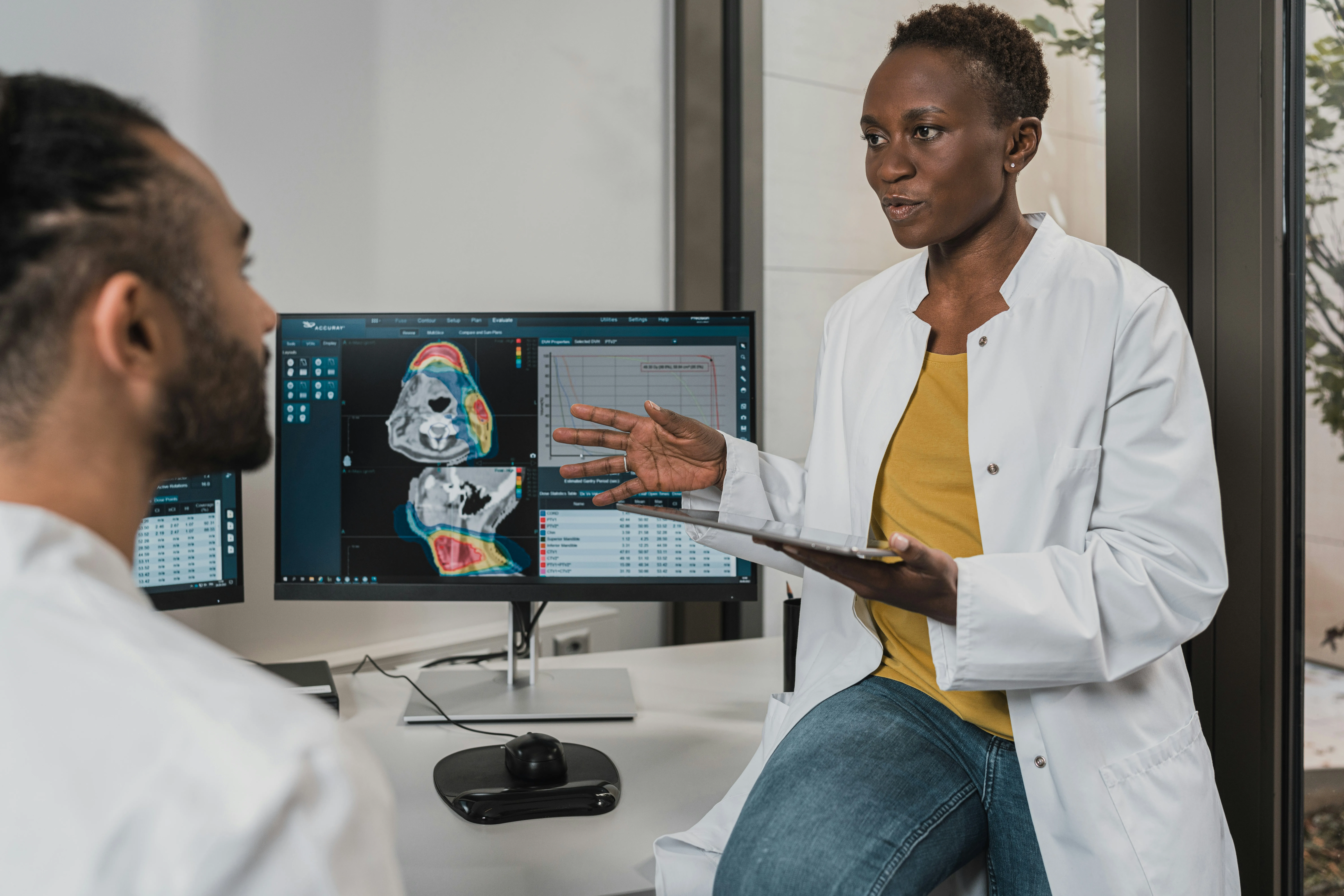 Two clinicians in white coats discussing diagnostic scans and result charts on a monitor.
